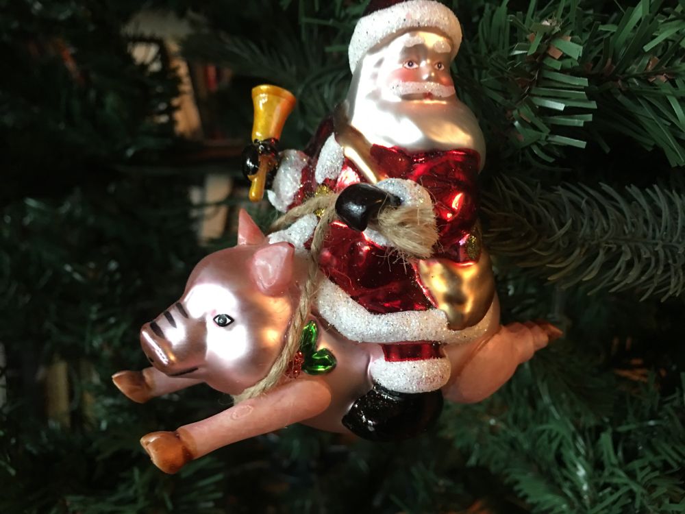 Blown glass flying pink pig with a Santa Claus on his back wearing a gold bag and ringing a gold bell