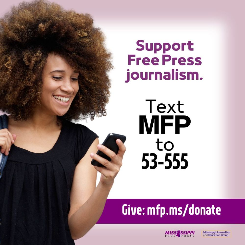 Lady with large Afro is wearing a black shirt. She is holding a phone in her left hand and she’s holding the strap to her purse on her shoulder with her right hand. 