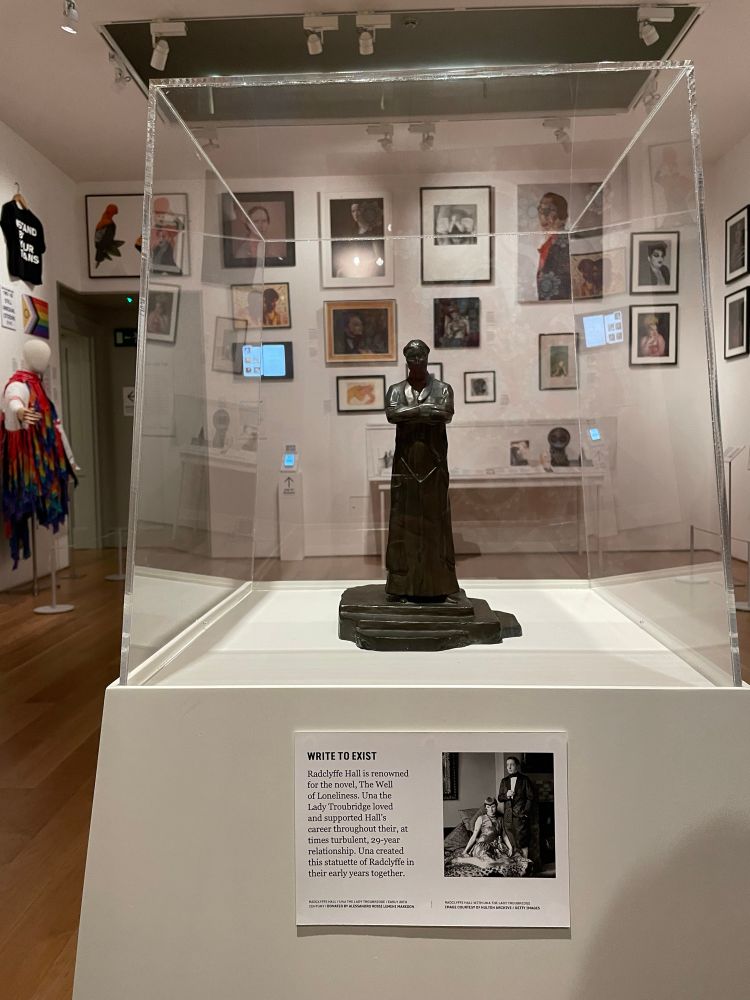 Miniature statue of Radclyffe Hall made by her partner Alice B. Toklas in a glass case in front of framed posters and other artefacts at the museum Queer Britain in King‘s Cross.