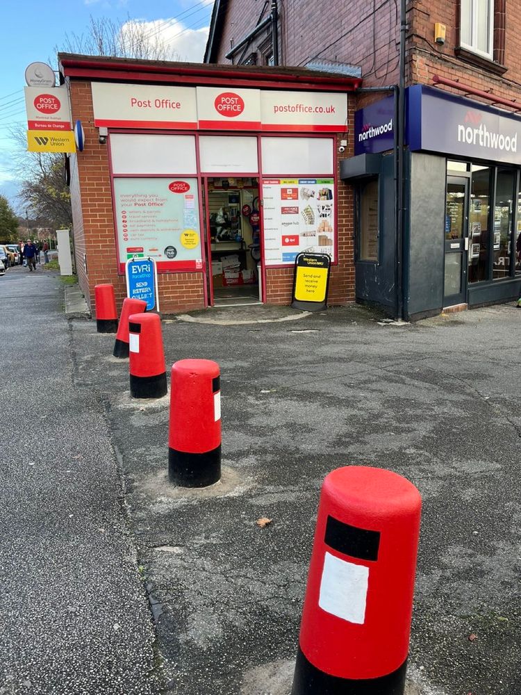 A row of postbox painted bollards in front of a post office.
