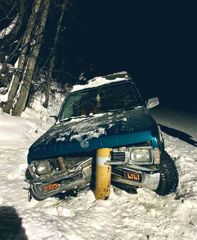 A big American truck meets a yellow bollard head on in a very snowy scene.