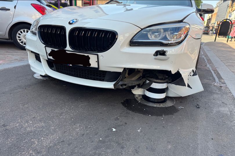 A white BMW crashes into a black and white bollard.