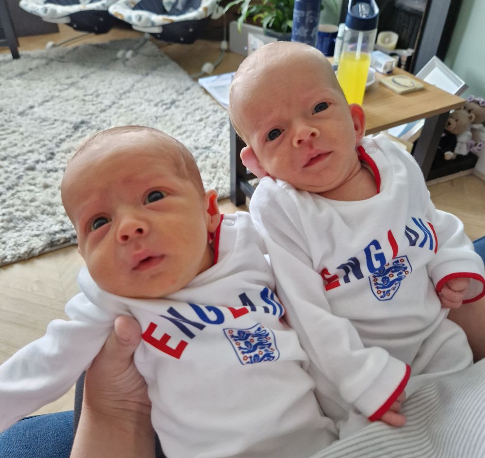 Two baby boys wearing white babygrows with the word England and the Three Lions logo