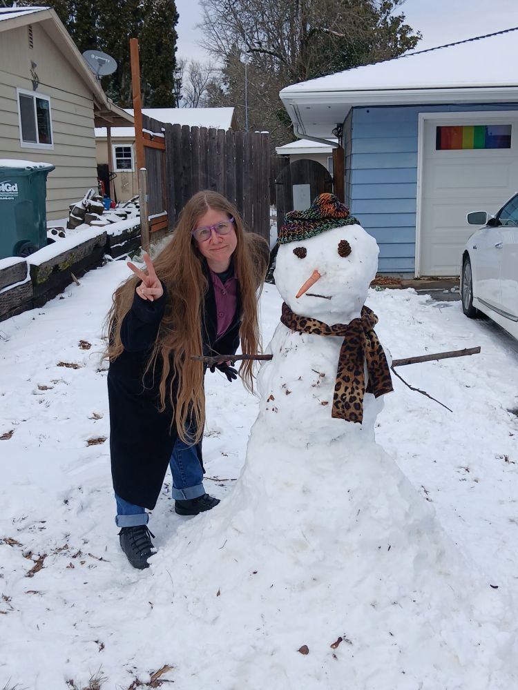 A woman in a huge black coat beside a snow person