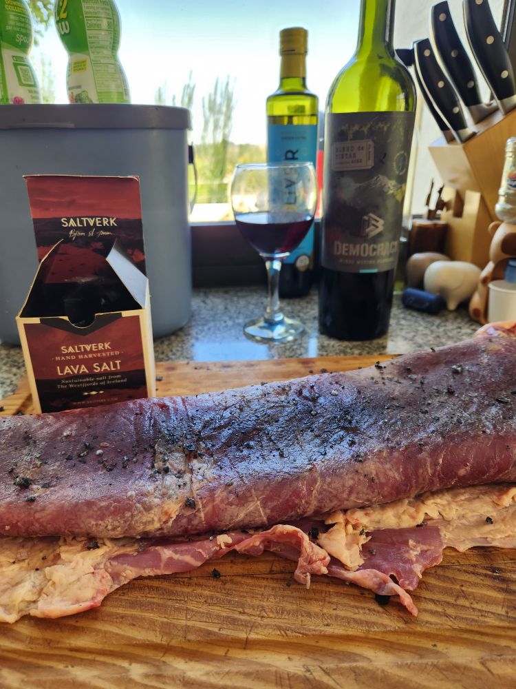 Photo of a piece of meat (matambre) salted with "lava salt" and in the background a glass and bottle of the delicious democracy wine