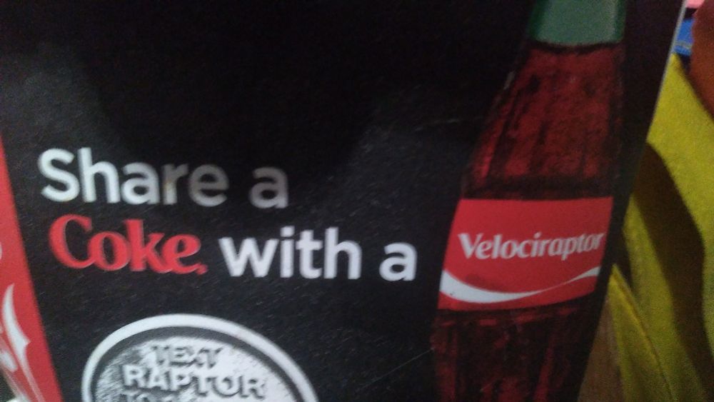 A cut-out section of soda cup bearing the text "Share a Coke with a Velociraptor".