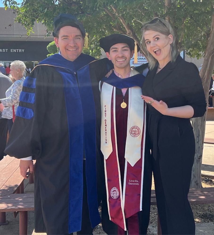 Three academics standing, two in garb