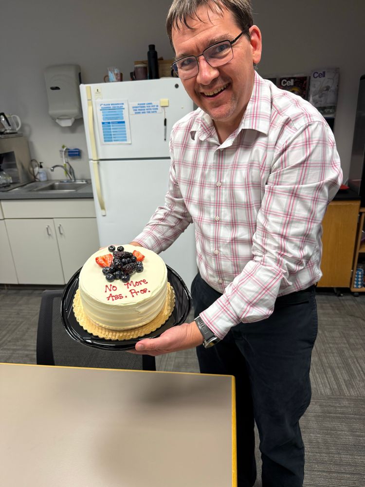Newly anointed full professor holds cake storying his past appointments.