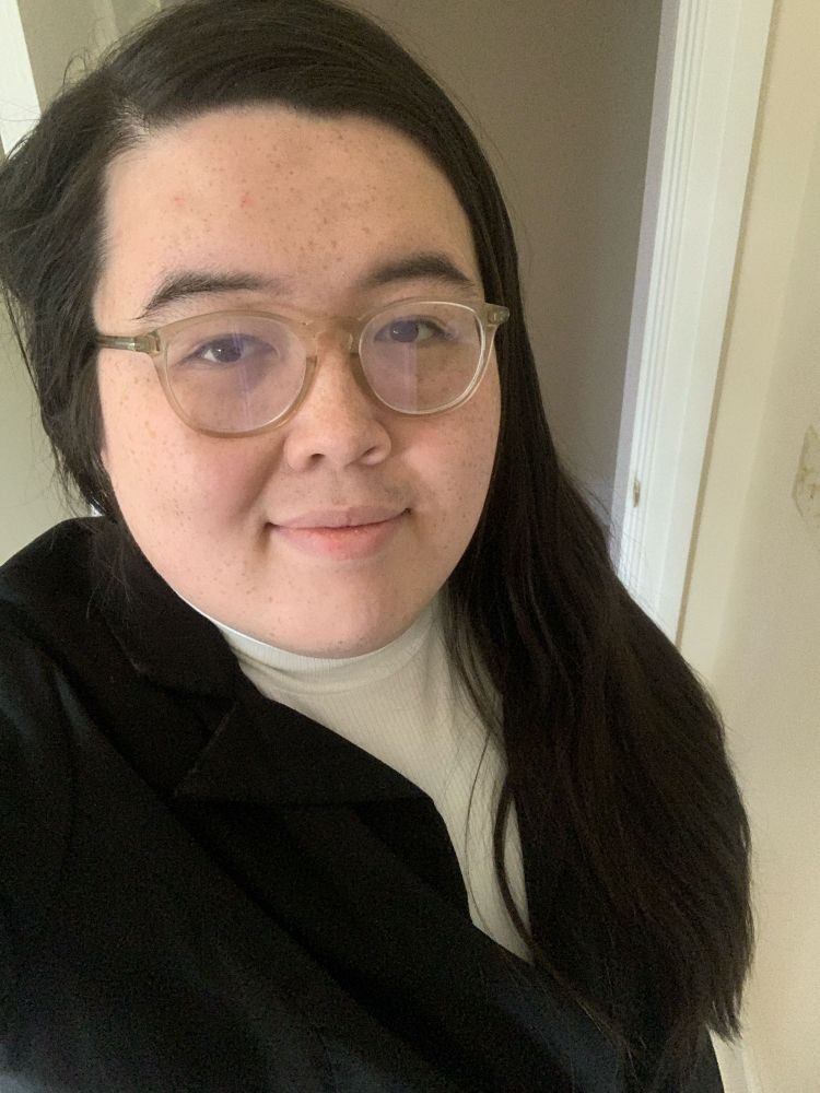 Zoey, a half-Filipino and half-white woman, wearing a white turtleneck shirt with a light suit jacket on top.