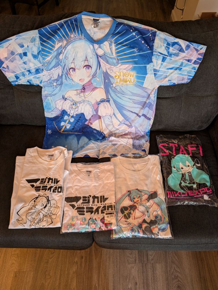 Unfolded shirt is the Snow Miku 2019 full graphic (not worn, JP XL). Folded shirts left to right: Magical Mirai 2018 Flash Color shirt (not worn, JP XL), Magical Mirai 2018 Event T shirt (not worn, JP XL), Unknown Miku Expo T-Shirt (Maybe Taiwan or Hong Kong?) (not worn, L), Miku Expo 2014 Staff T-shirt (RARE, not worn, XL)
