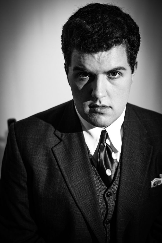 Hank Nelson looking into the camera with a straight face. Wearing a sportcoat vest and polka-dot tie