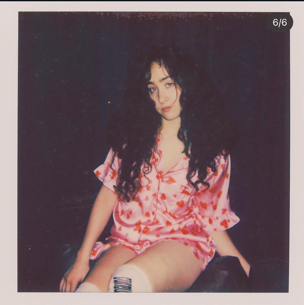 chappell roan polaroid from her insta, she’s wearing a pink pj set with red hearts all over it with her hair down & curly. 