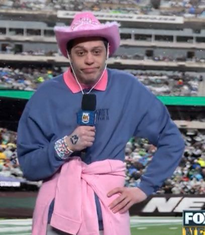 Pete Davidson dressed up fully in Taylor Swift merch and a cowgirl hat with his hand on his hip