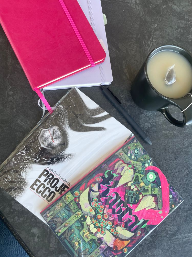 two notebooks, project ecco, rascal year one zine, a pen and a tea on a table