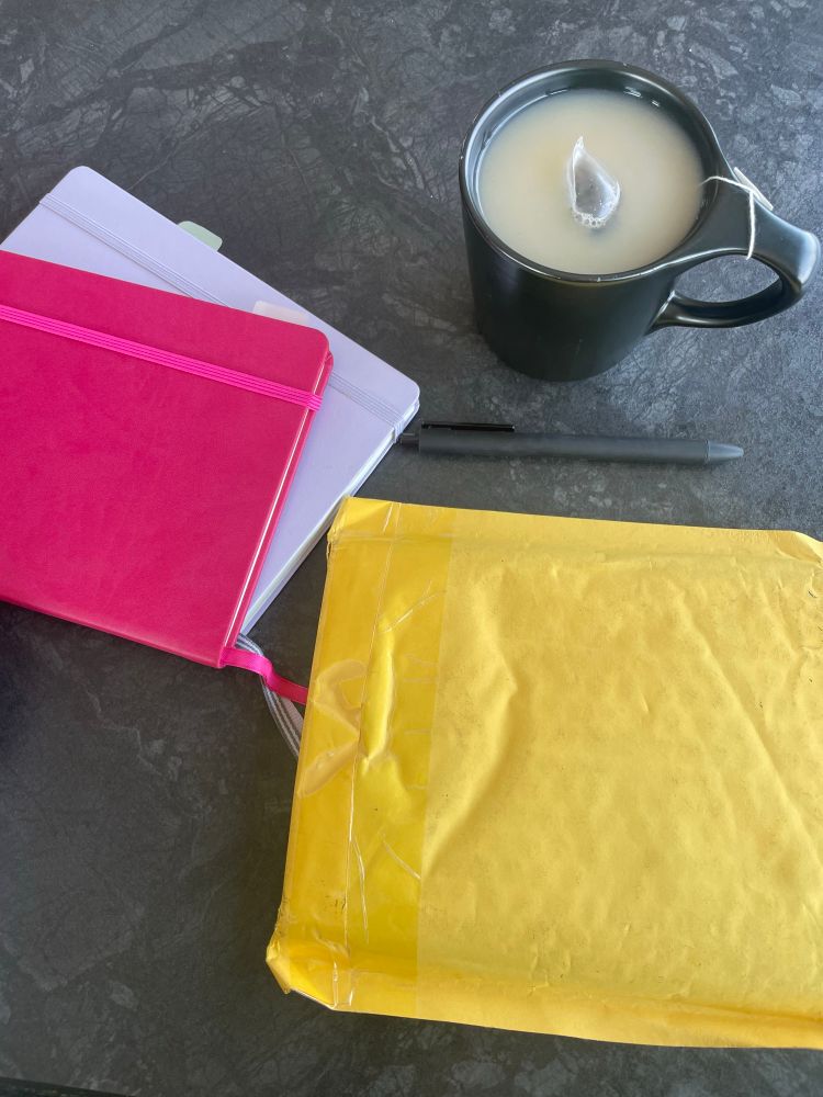 two notebooks, a tea, a pen, and a package on a table