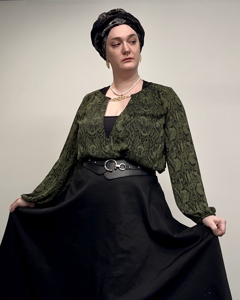 A white woman in a green snakeskin print blouse a big black skirt and a black headscarf