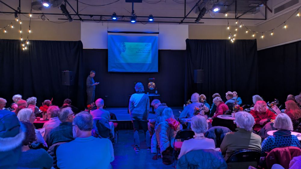 A dimly lit black box theatre with a crowd getting seated