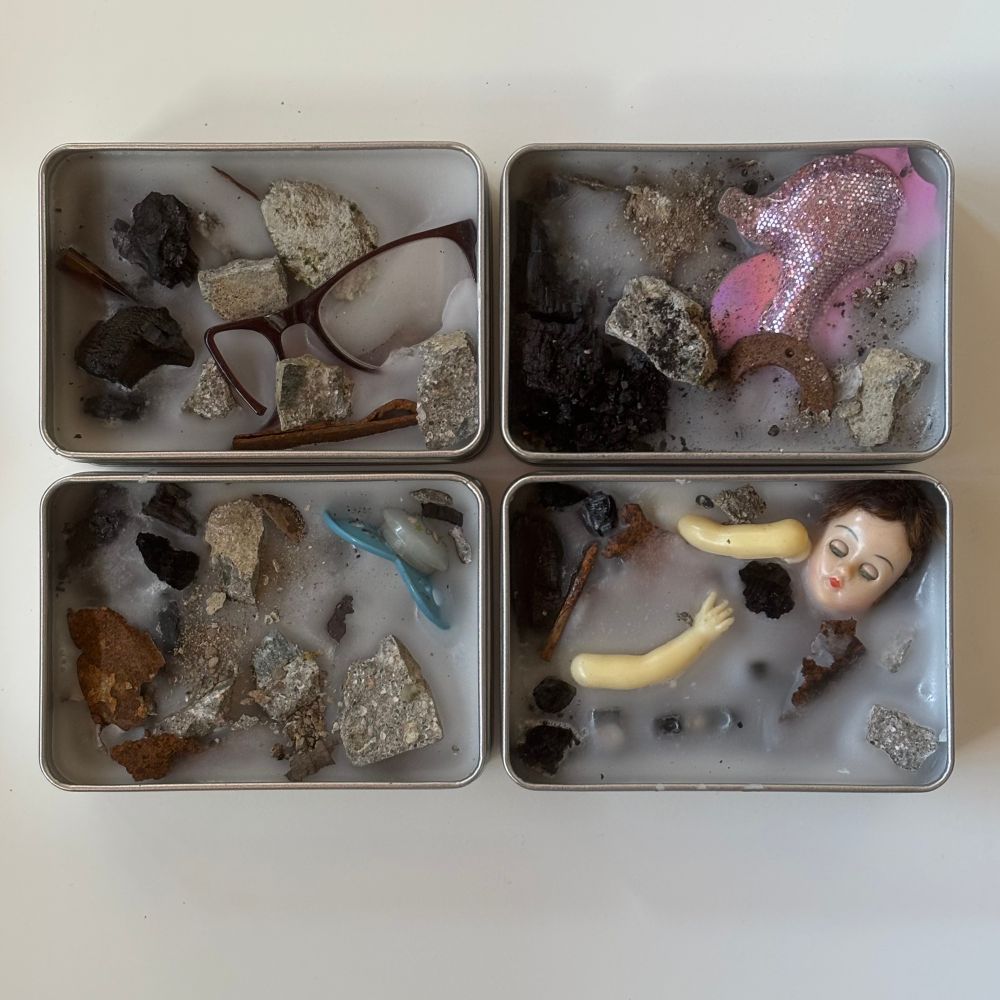 Four tin boxes holding mixed media artworks made from rubble, burnt wood and found objects embedded in wax. 