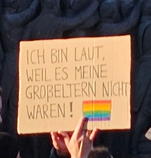 Pappschild
Ich bin laut, weil es meine Großeltern nicht waren! Dahinter eine gemalte Regenbogenfahne