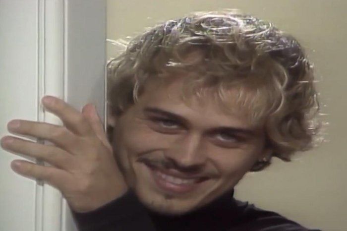 Foto do Alexandre, de "A Viagem", sorrindo de forma visagenta enquanto tá num cantinho observando.