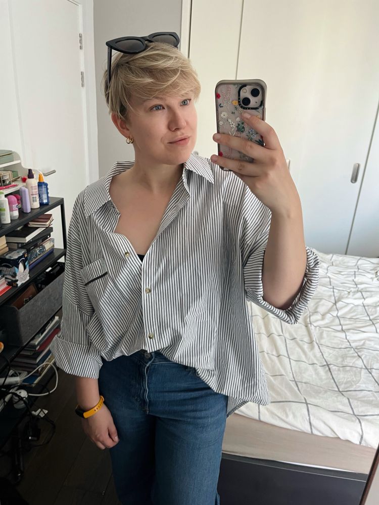 Selfie in a mirror. I’m wearing wide leg blue jeans, and a white striped very oversized shirt, gold earrings, and a dorky yellow Fitbiton my wrist