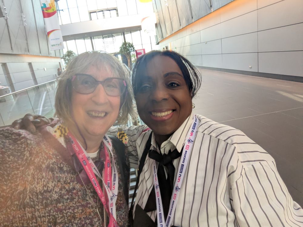 Lisa, a white grey haired woman in a hand-knitted jumper with Maxine a black woman wearing a white top with thin black stripes and a black bow at the collar 