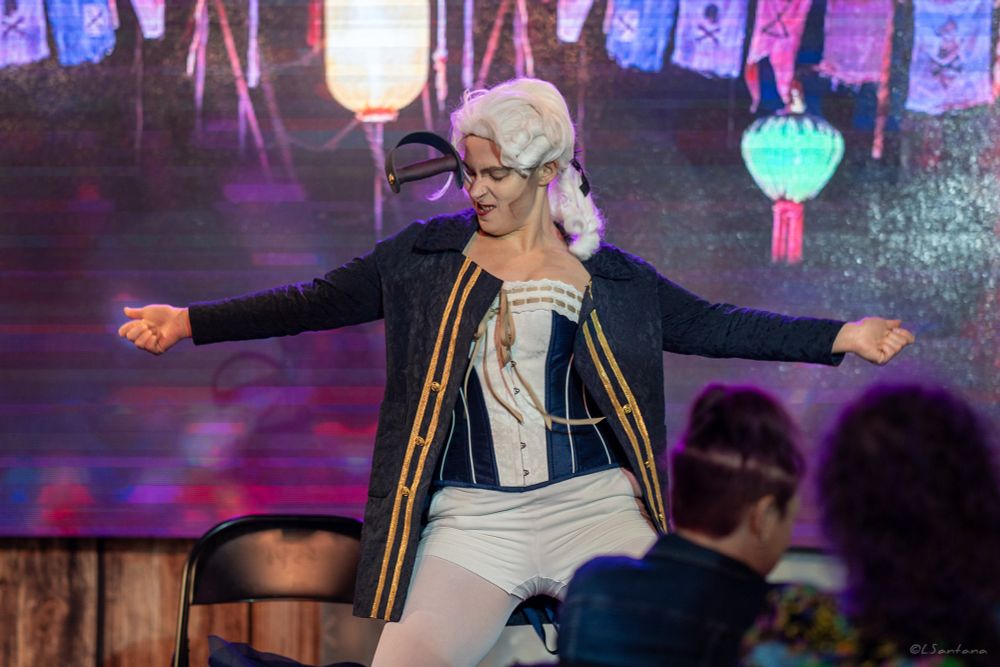 Polly Cocktail dances on stage in drag as Nigel Badminton. 