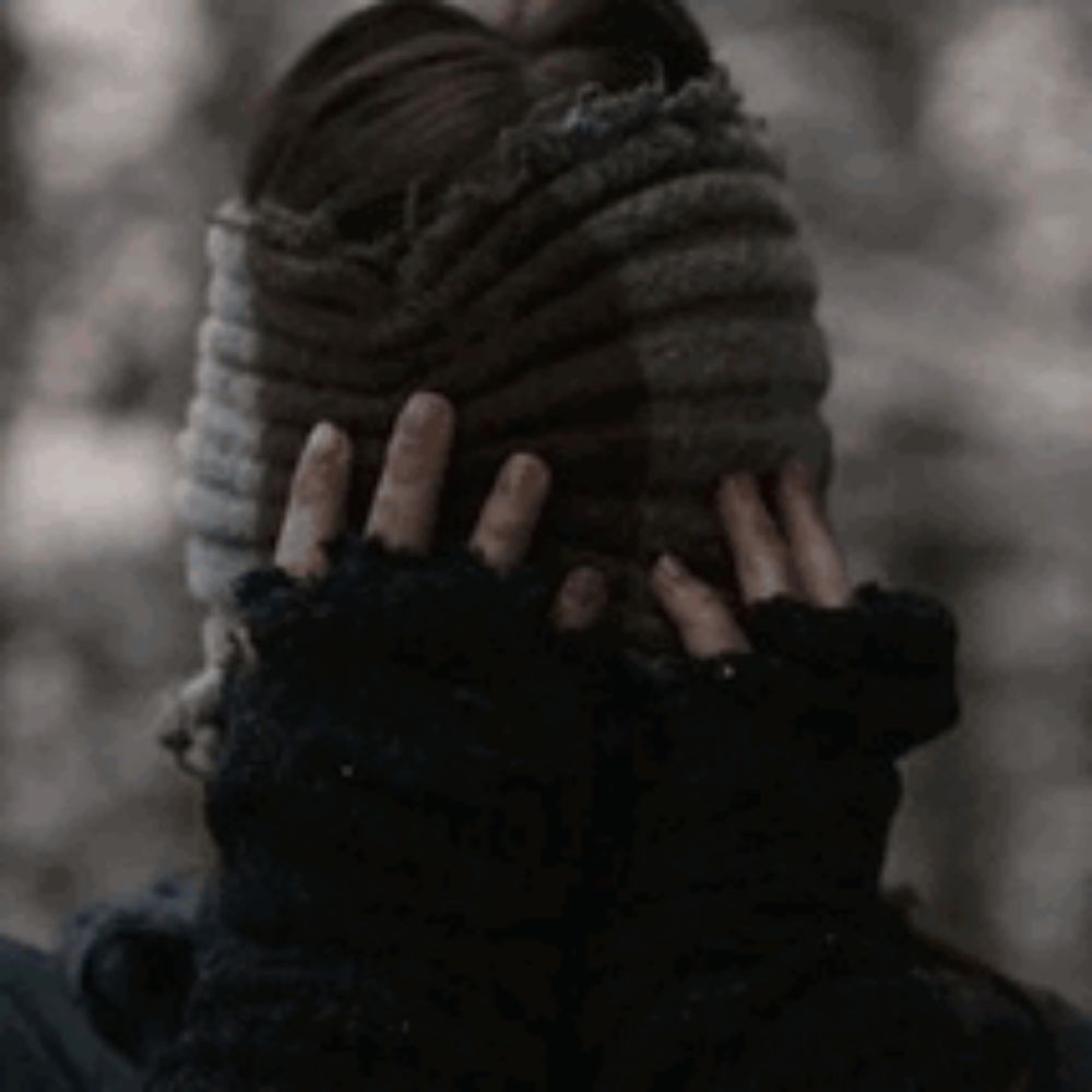 a person wearing a knitted hat and gloves is covering their ears with their hands .