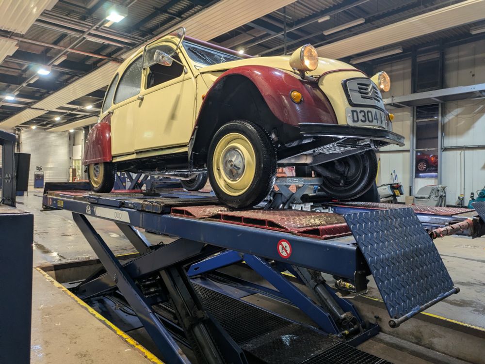 A plum and custard Citroen 2CV on a vehicle inspection ramp