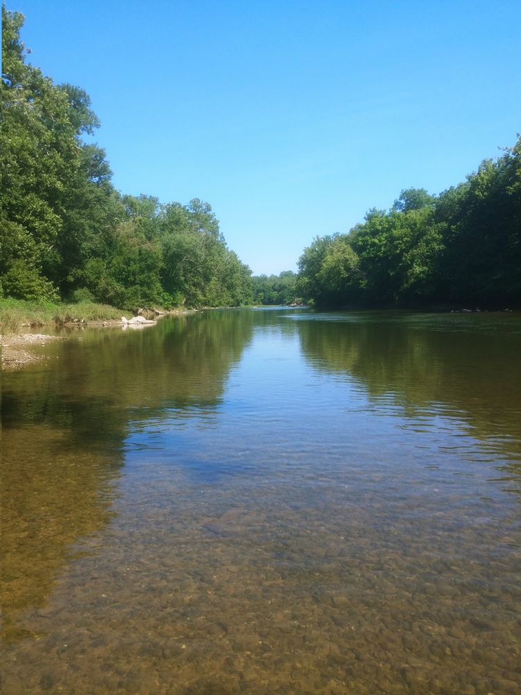 A river with trees on both sides, and with the trees and the blue sky reflected in the river.