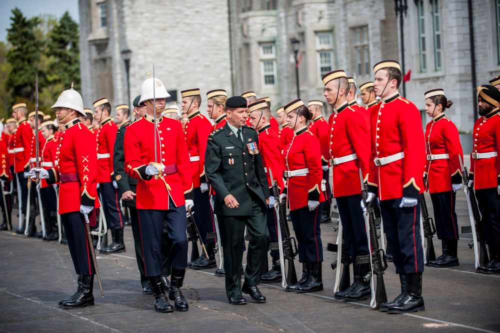 Canadian Royal Military College cadets in scarlet uniforms being inspected by a senior Canadian Army officer. 