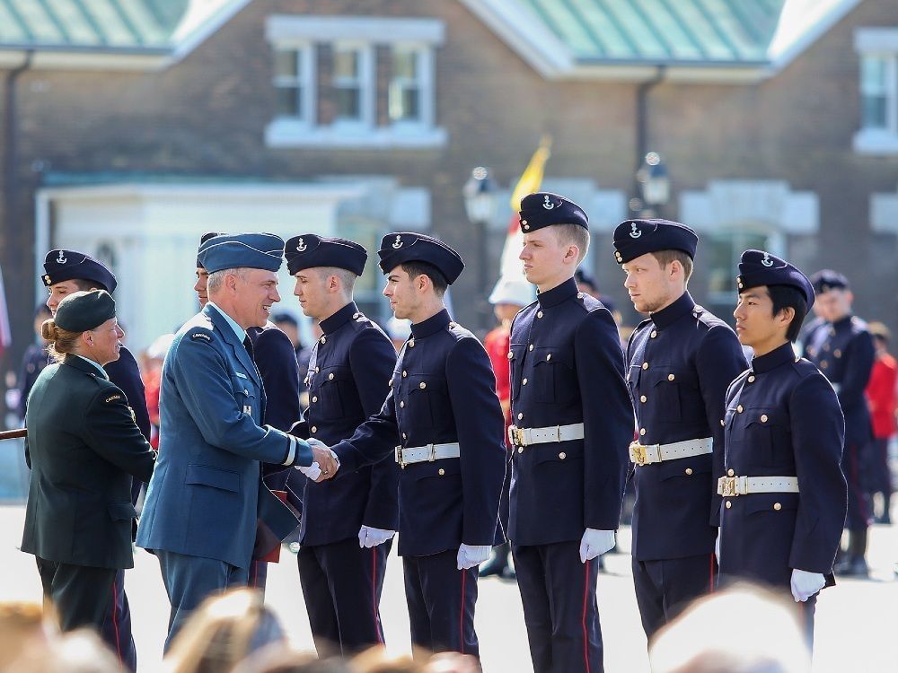 Canadian Royal Military College cadets in blue uniforms being inspected by a senior Royal Canadian Air Force officer. 