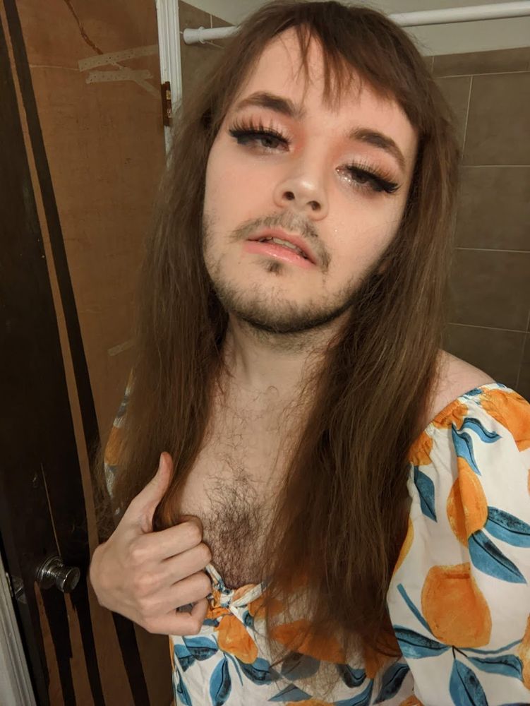 brunette woman with a little bit of facial hair, kinda slaying in a peach-themed dress