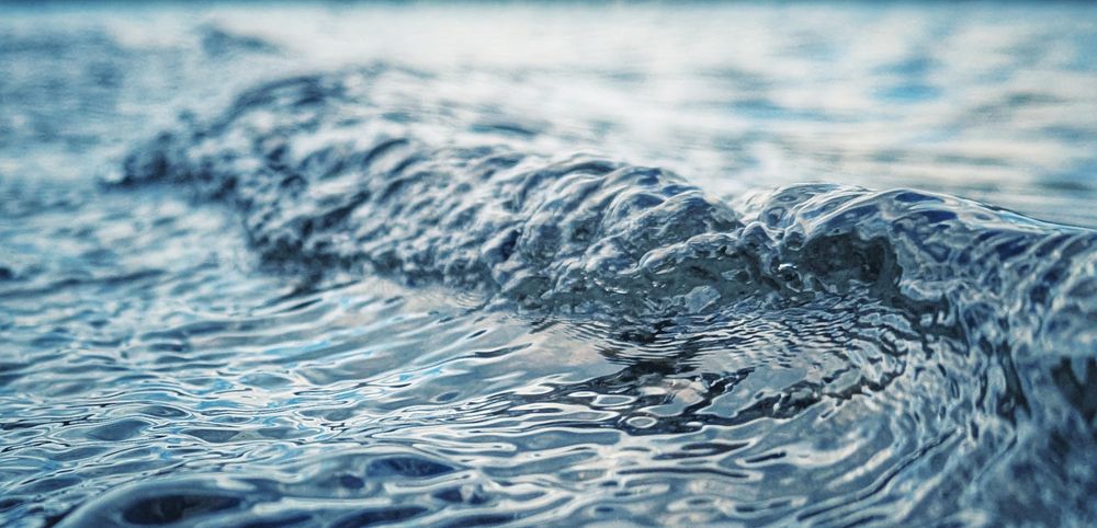 Foto einer winzigen Welle im Wasser, die gerade umschlägt.