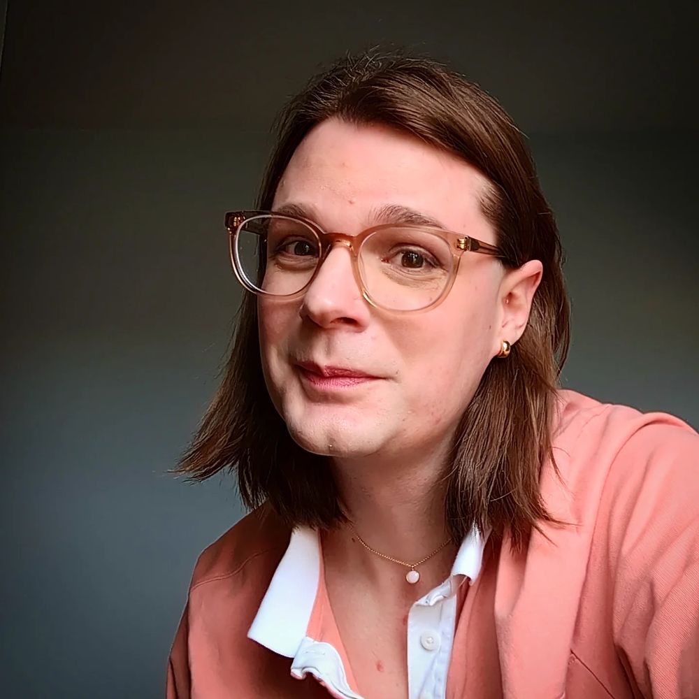 Zoraphel wearing a pink shirt, pink glasses, pink necklace, pink lipstick