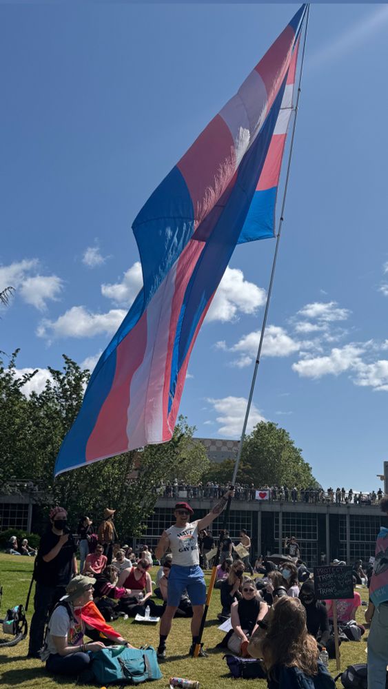 Aj holding a giant trans flag at the Seattle Center after the No Kings protest