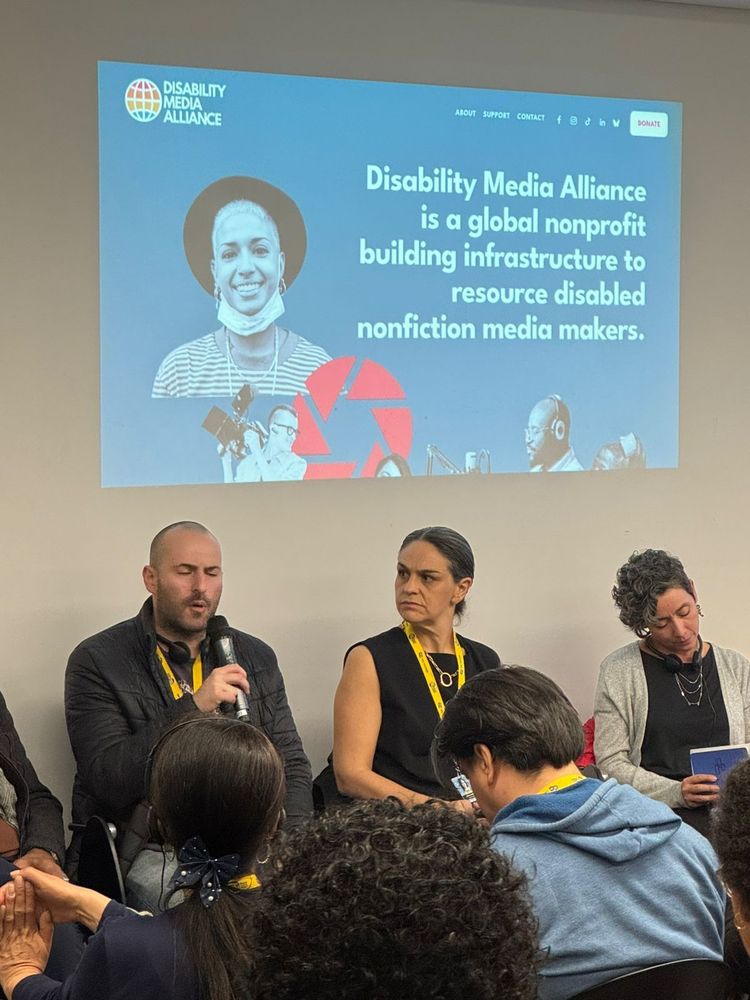 Panelists speak in front of a projected slide that reads: “Disability Media Alliance is a global nonprofit building infrastructure to resource disabled nonfiction media makers.” Audience members are visible in the foreground.
