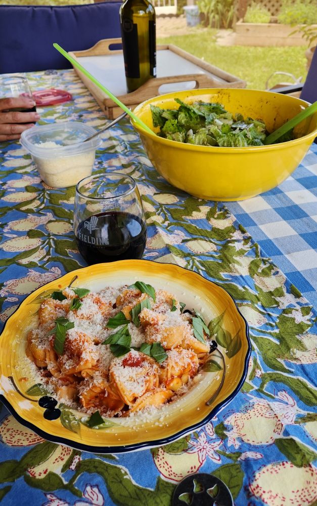 Picture of a plate of pasta with parmesan cheese and basil on it, with a large yellow bowl full of salad behind it.