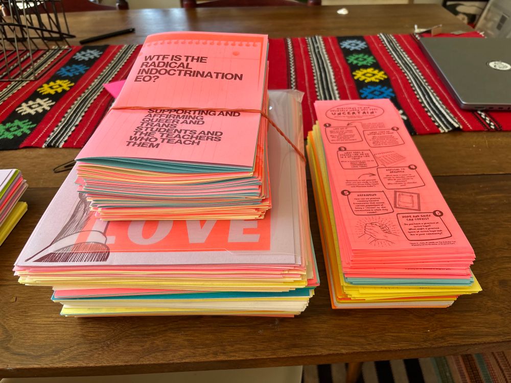 Multiple stacks of hundreds of brightly risograph printed materials for distribution including my zine for supporting and affirming queer and trans students and their teachers and the “what to do when you feel uncertain” pamphlet. 