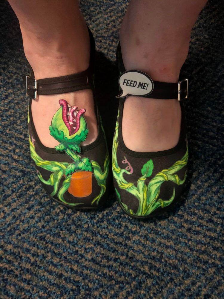 Black shoes with an Audrey 2 style plant on one and a speech bubble that reads 