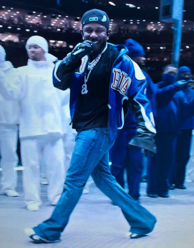 Kendrick staring like a menace directly into the camera he has a thick chain with a big a on it 