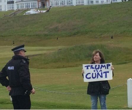 A woman with a sign saying trump is a cunt the police are walking towards her 