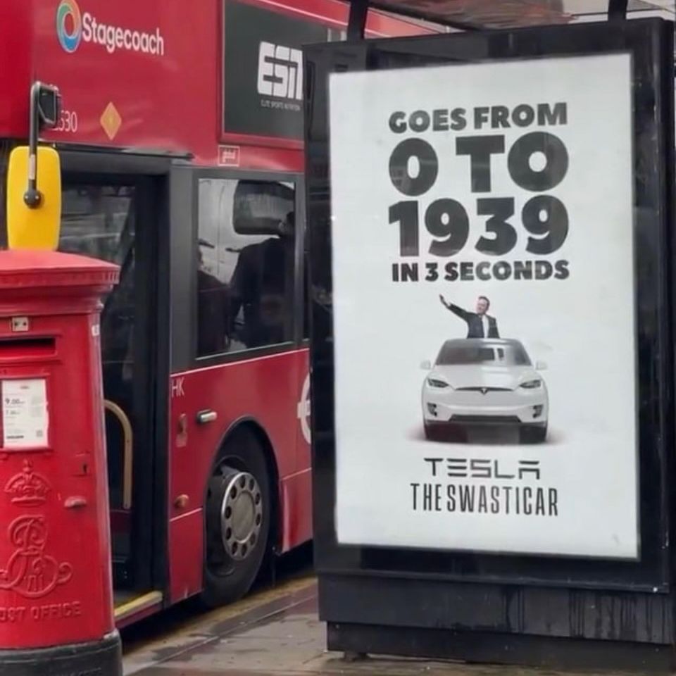 A bus shelter sign that says goes from 0 to 1939 in seconds Tesla the swasticar a picture of a Tesla and Elon musk doing a Nazi salute 