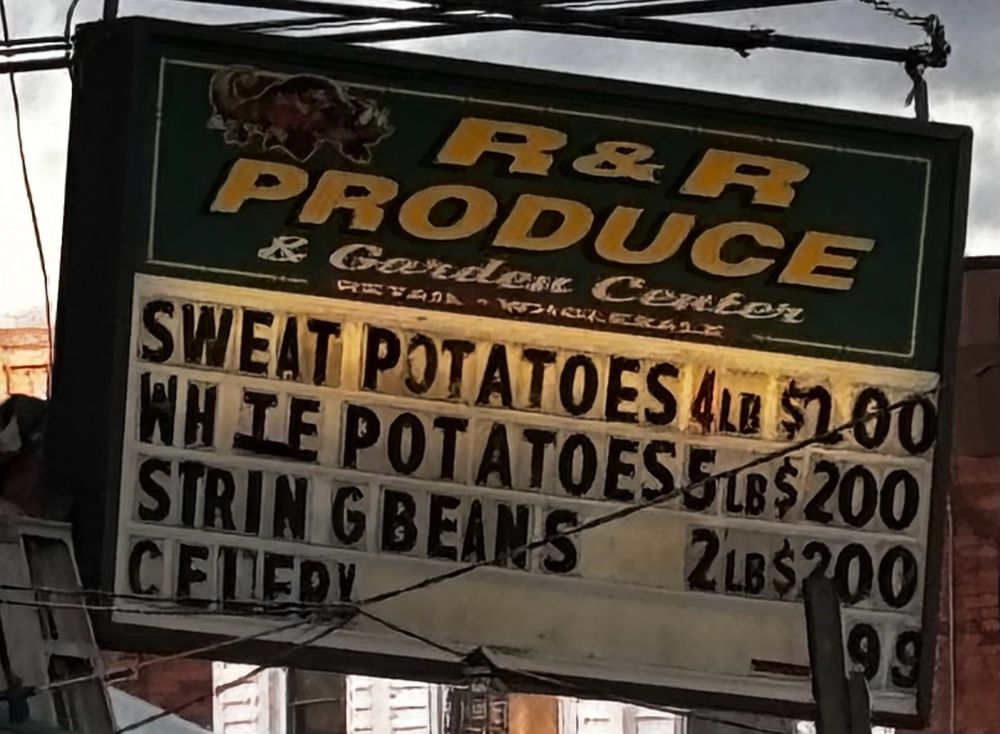 a storefront grocery's sign offering "sweat potatoes" and "whie potatoes"