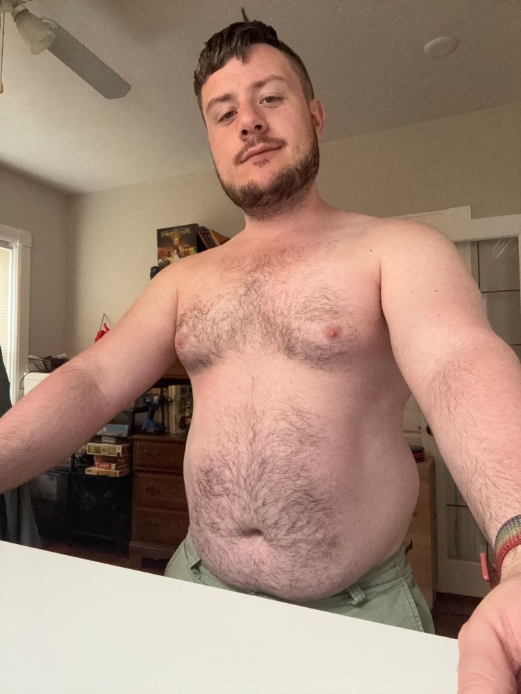 MuscleCubRook at his desk. He is in just shorts and showing off his belly