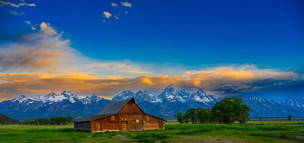 A view of the Moulton Barn in the foreground at sunrise with the Grand Tetons in the background. At Grand Teton National Park
