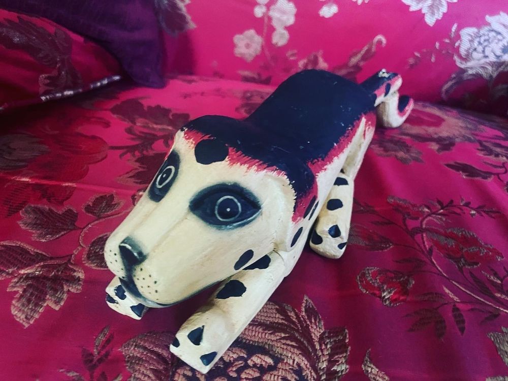 another close up shot of the small wood carved dog on a decorate fabric chaise lounge 