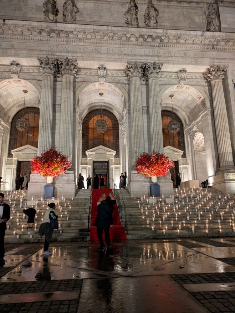 The new york city public library lit up with candles and a red carpet in the rain. 
