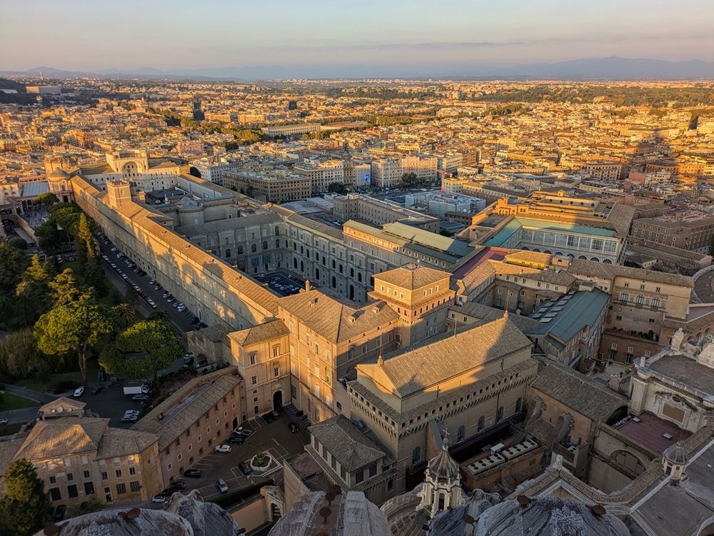 A view from above of part of Vatican City and Rome at sunset, showing in particular a large building, the Cortile del Belvedere.