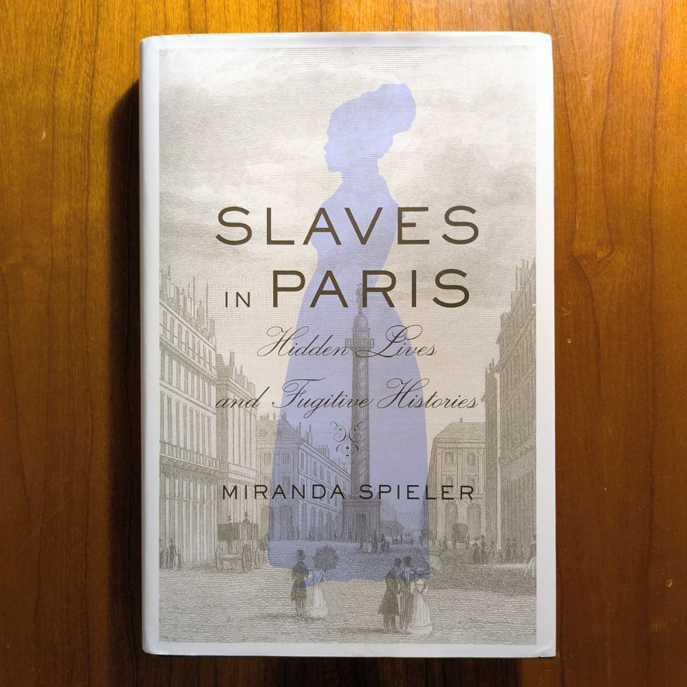A photograph showing a copy of a book, "Slaves in Paris", on a brown wooden desk.